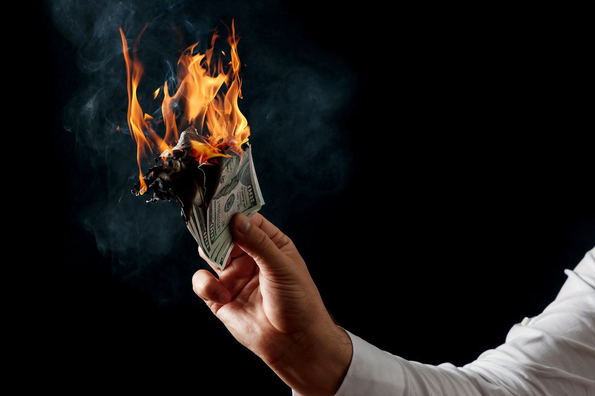 Hand holding a wad of 100-dollar bills set ablaze.