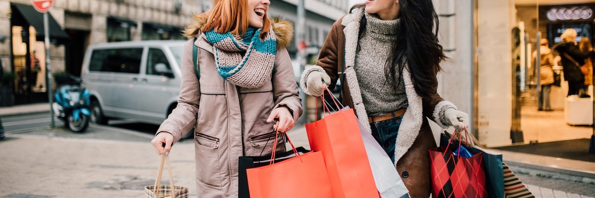 A couple of young women crossing the street and carrying a massive number of shopping bags.