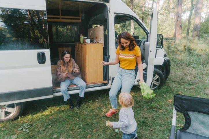 Two women and a child smile as they play outside their camping van.