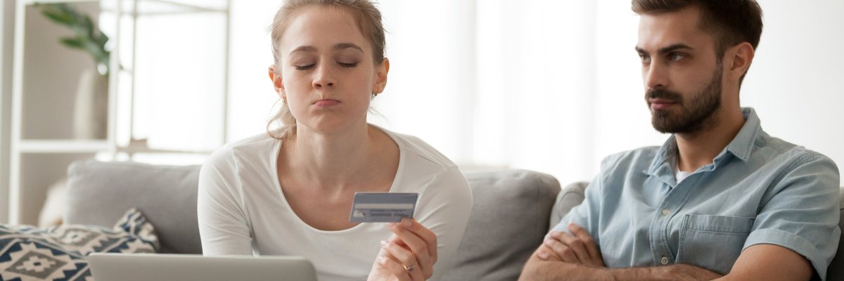 Man sulking as woman beside him pouts while holding a credit card.