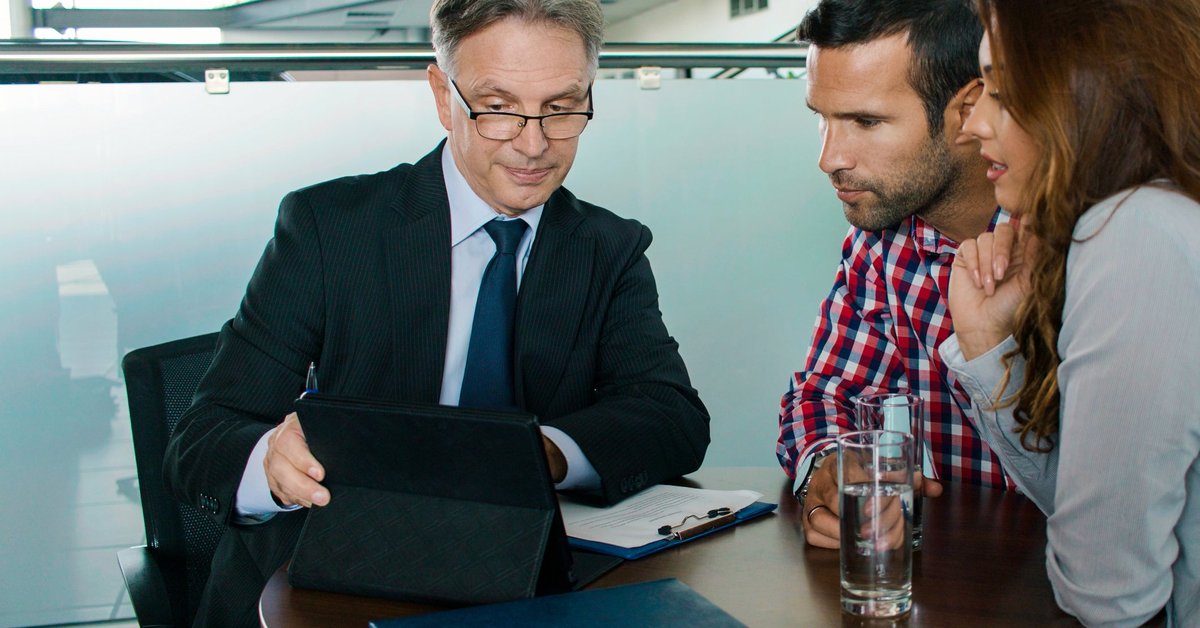 A couple meets with a financial advisor, looking concerned at a tablet screen.