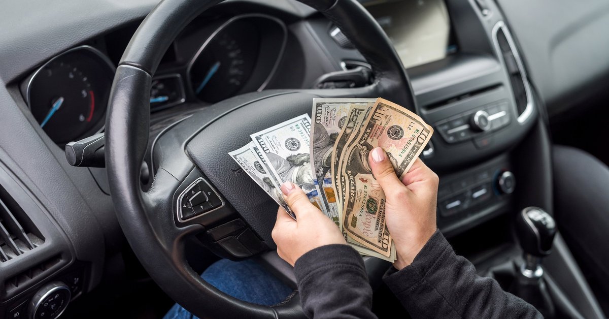 Pair of hands belonging to person sitting in driver's seat of car flipping through a wad of cash.