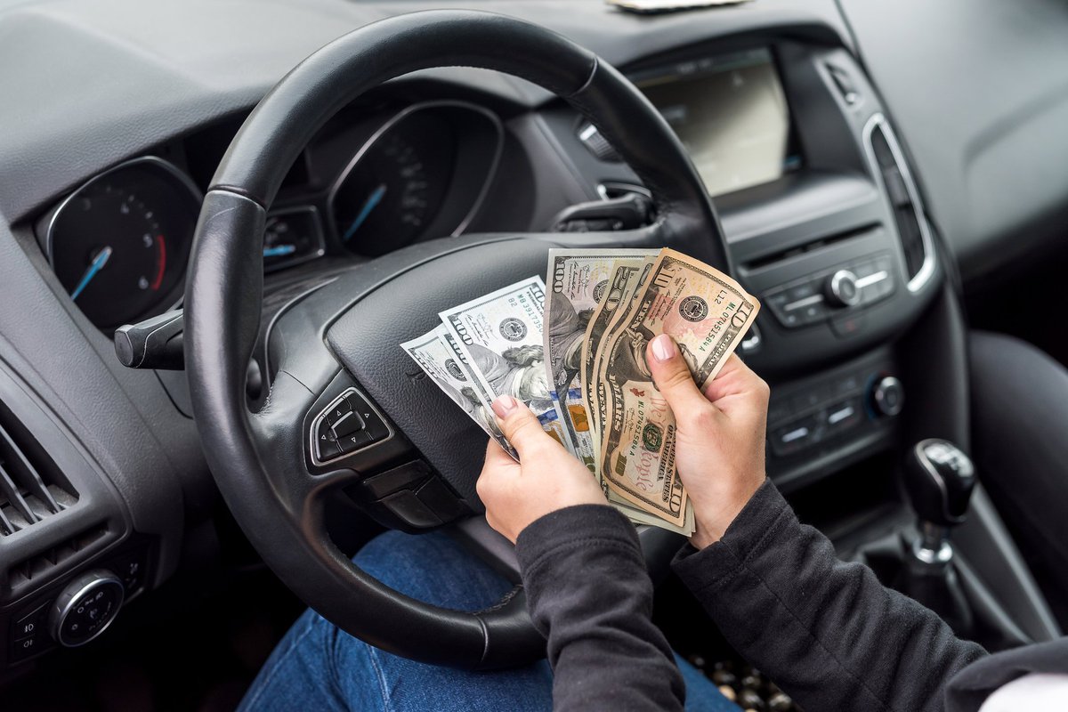 Pair of hands belonging to person sitting in driver's seat of car flipping through a wad of cash.