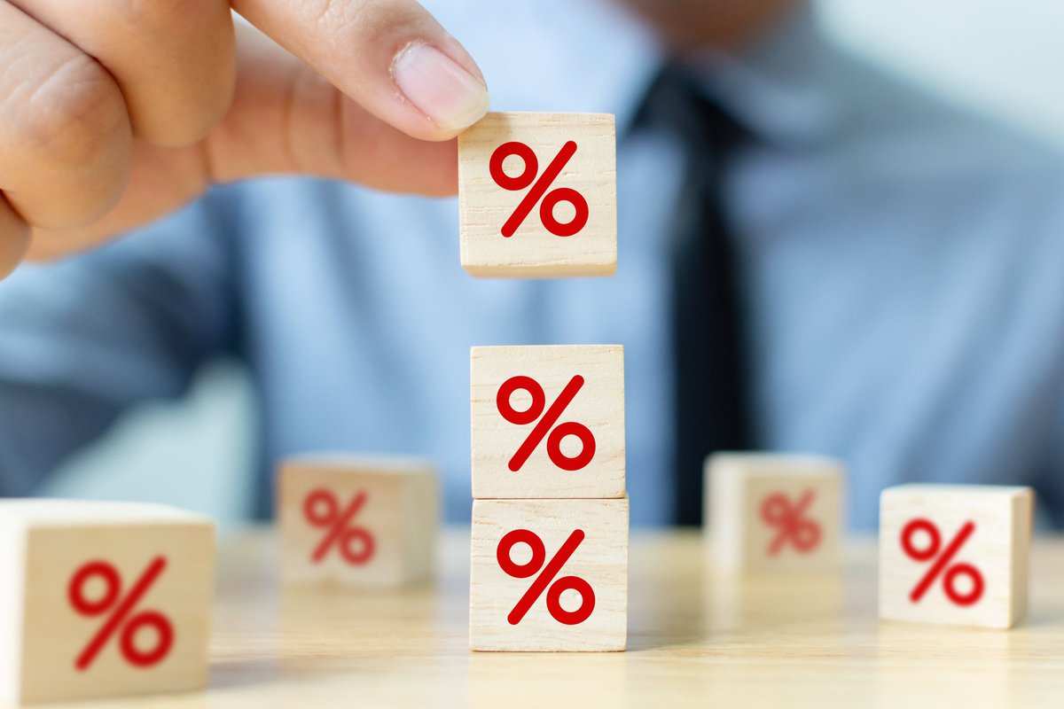 Person in shirt and tie stacking small wooden blocks painted with a red percentage sign.