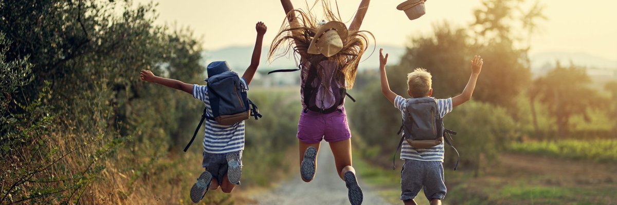 Three children leaping into the air on a gravel path somewhere in nature.