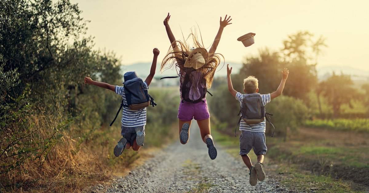 Three children leaping into the air on a gravel path somewhere in nature.