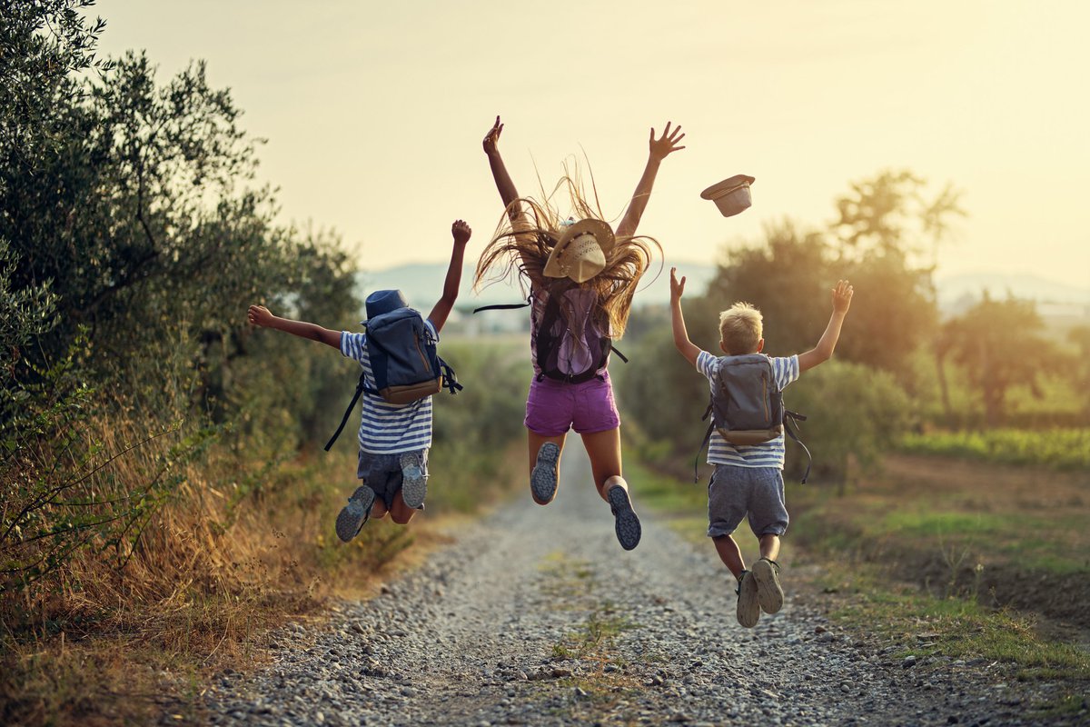 Three children leaping into the air on a gravel path somewhere in nature.
