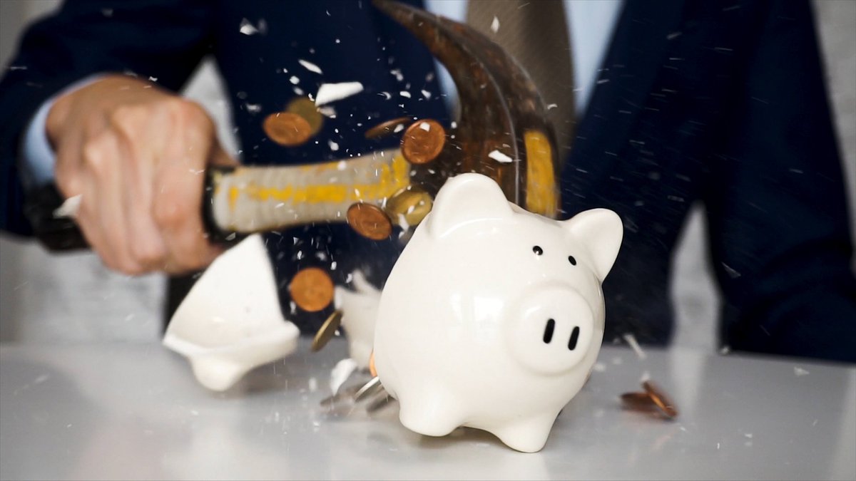 Man in suit shattering piggy bank with hammer.