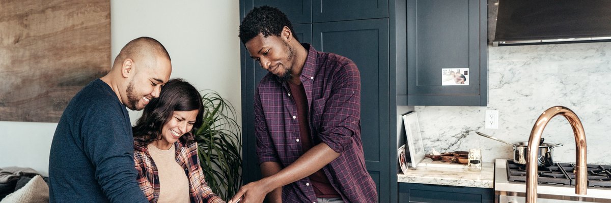 A family meets with a realtor, who points at paperwork and smiles in a kitchen.