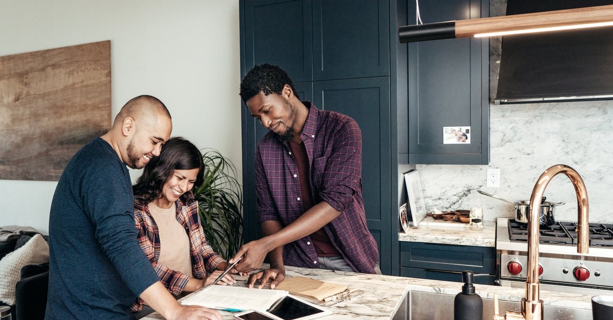 A family meets with a realtor, who points at paperwork and smiles in a kitchen.