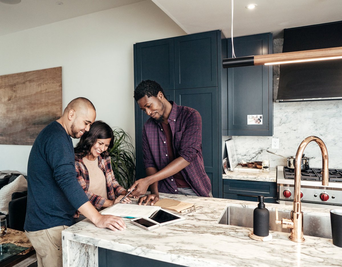A family meets a realtor who points to papers and smiles in the kitchen.