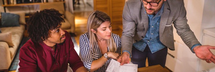 Three people discuss finances while filling out paperwork in their home.