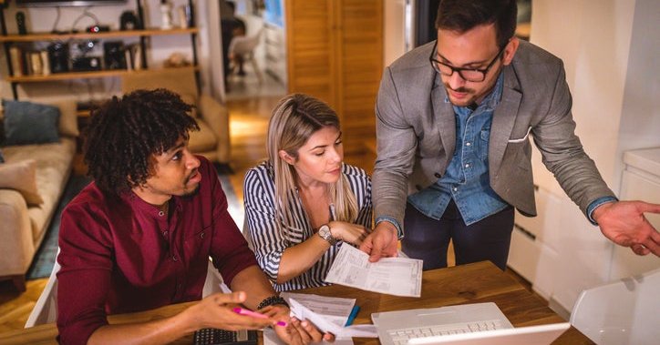 Three people discuss finances while filling out paperwork in their home.