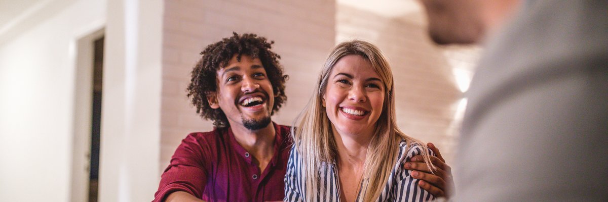 A couple happily shakes hands with a real estate agent in an office.