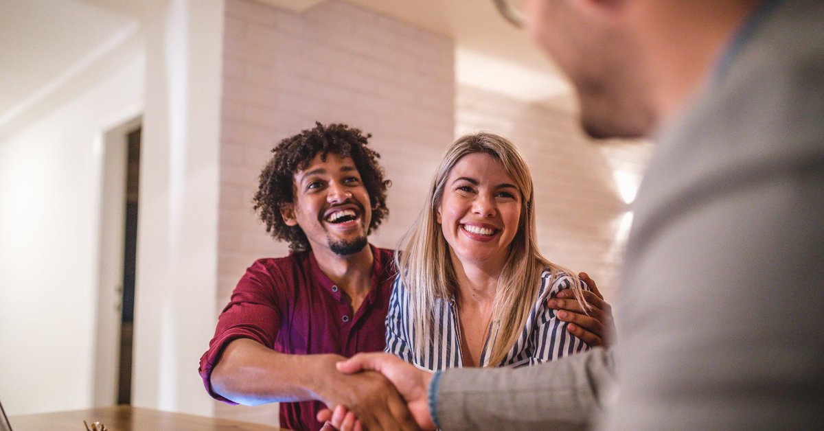 A couple happily shakes hands with a real estate agent in an office.