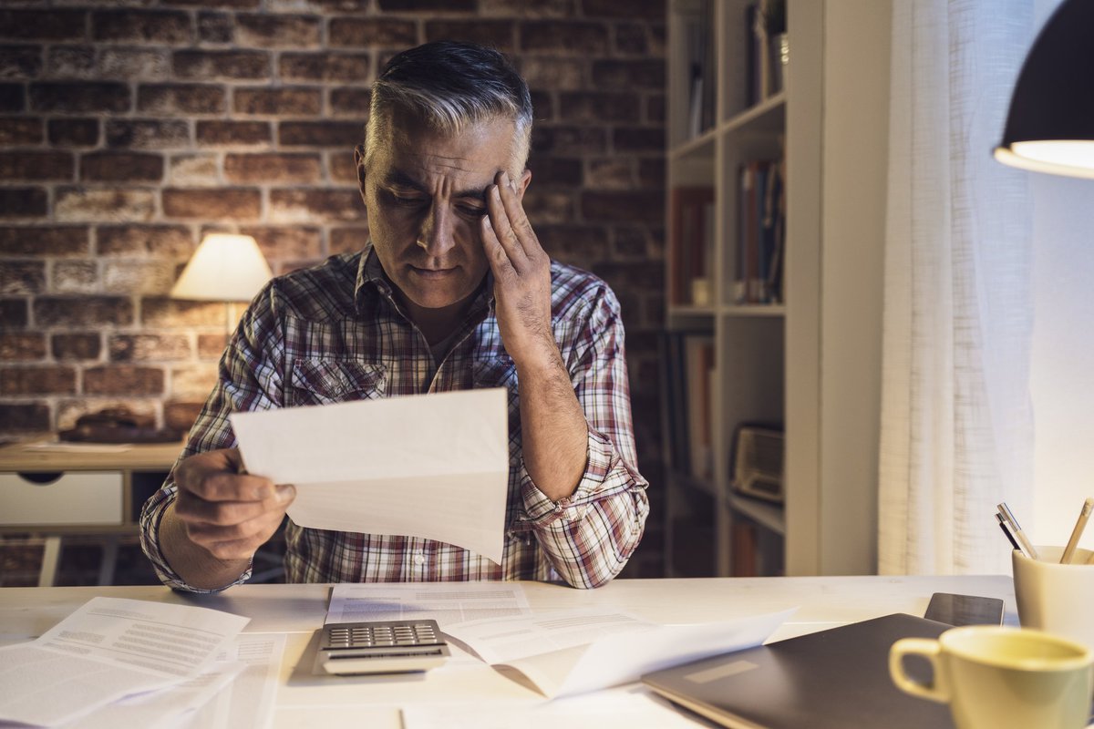 Middle-aged man suffering migraine headache caused by bills.