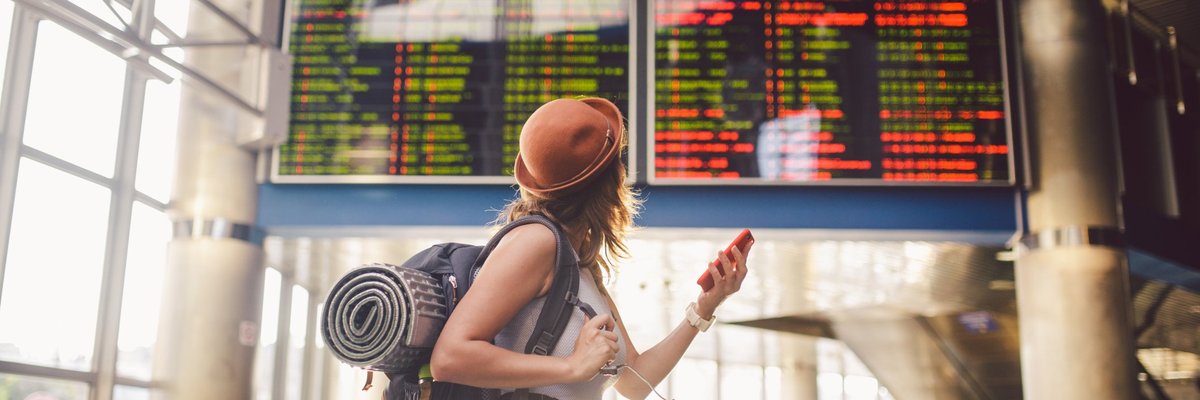 Young woman in airport looking up at flight information board.
