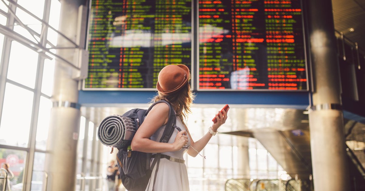 Young woman in airport looking up at flight information board.