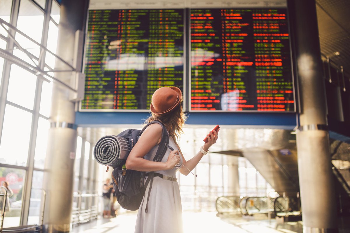 Young woman in airport looking up at flight information board.