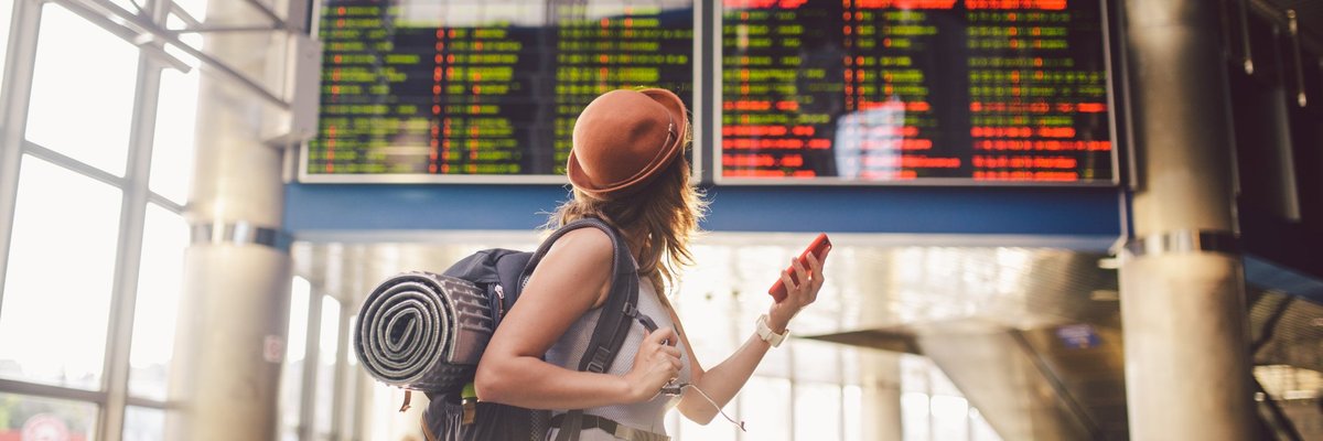 Young woman in airport looking up at flight information board.