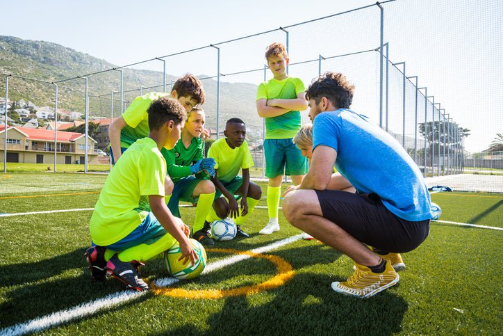 Adult male huddled with young soccer players.