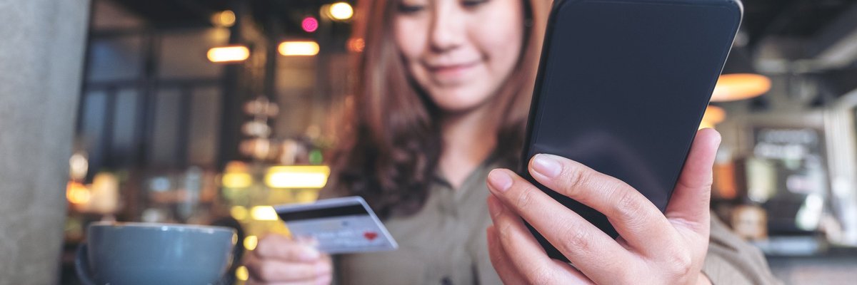 Young woman in coffee shop smiling at her credit card and phone.
