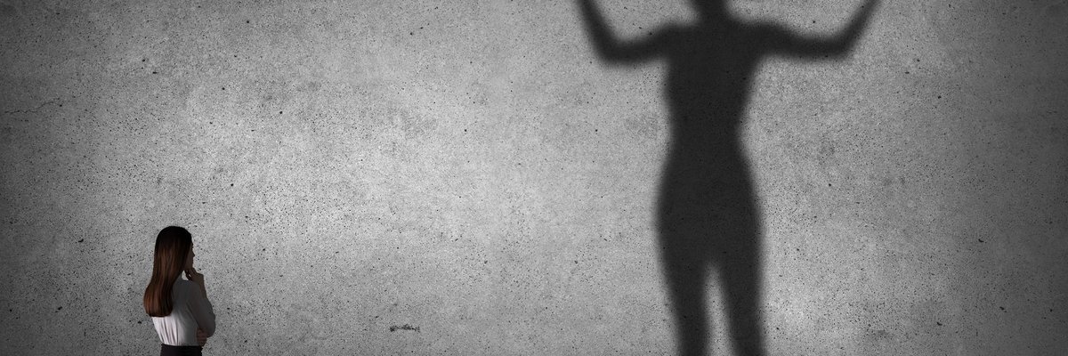 Woman looking at her much larger and stronger-looking shadow.