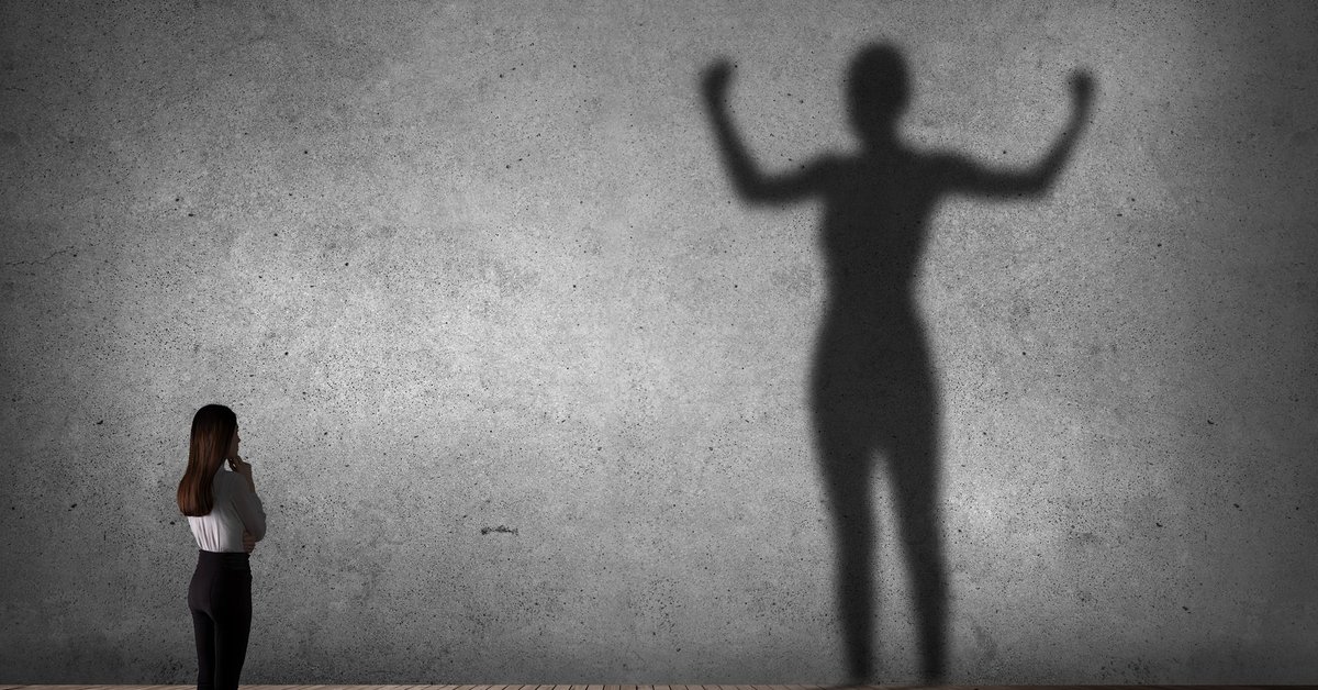 Woman looking at her much larger and stronger-looking shadow.