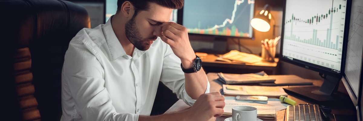 Young man sitting behind desk overrun with financial papers looking deeply stressed.