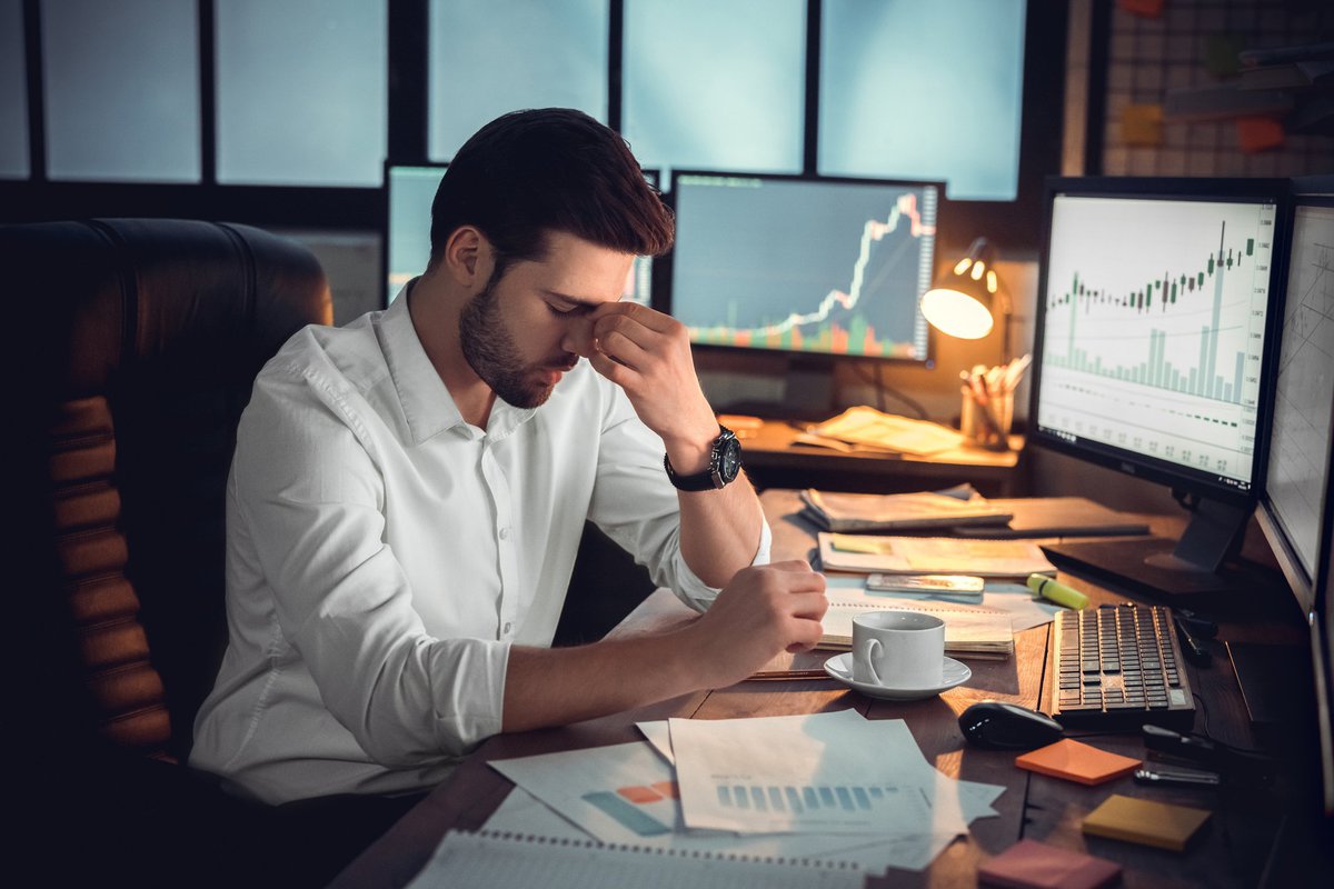 Young man sitting behind desk overrun with financial papers looking deeply stressed.