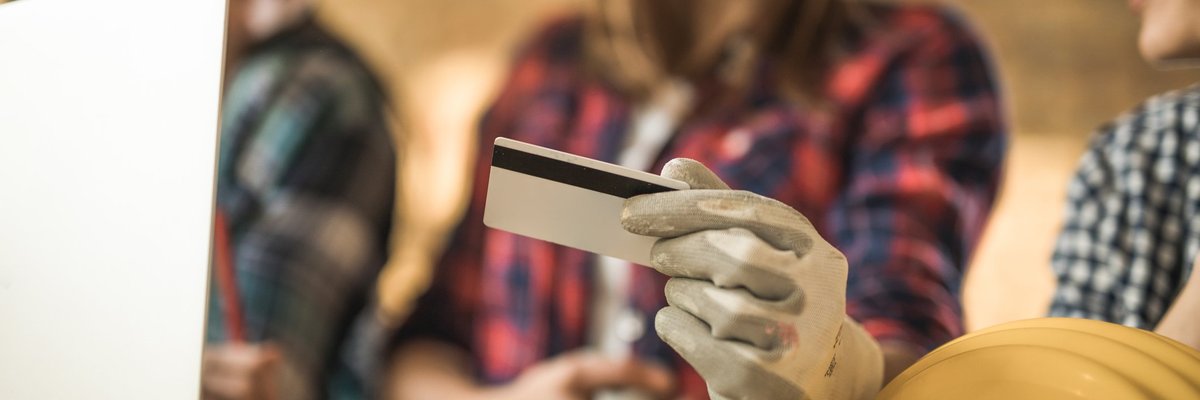 Trio of women in flannels and construction helmets looking at a credit card.