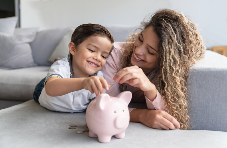 Young mother and small child smile while depositing coins into a piggy bank.