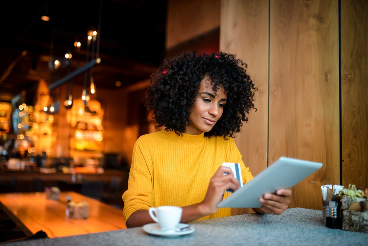 Young woman looking at a tablet with a credit card in hand.