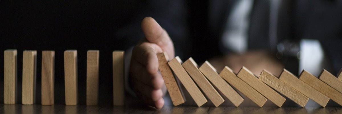 A hand interrupting a row of wooden dominos from continuing to fall over.