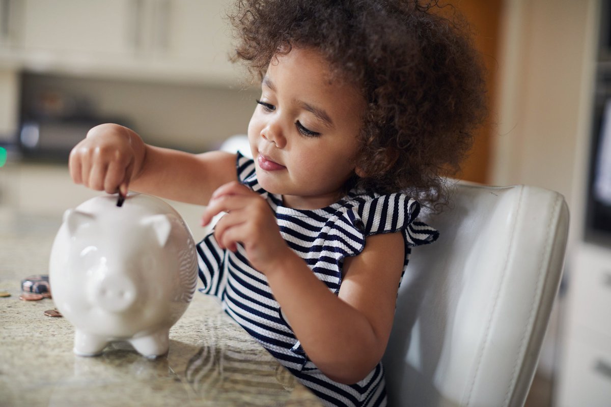 A child puts coins into a piggy bank at the kitchen table.