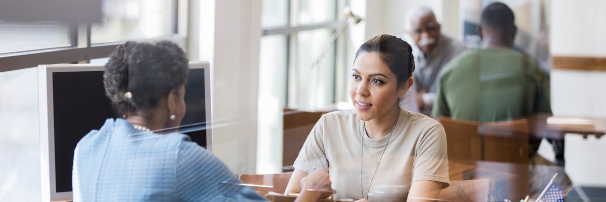 Two women sitting across a desk from one another in an office and discussing something important.