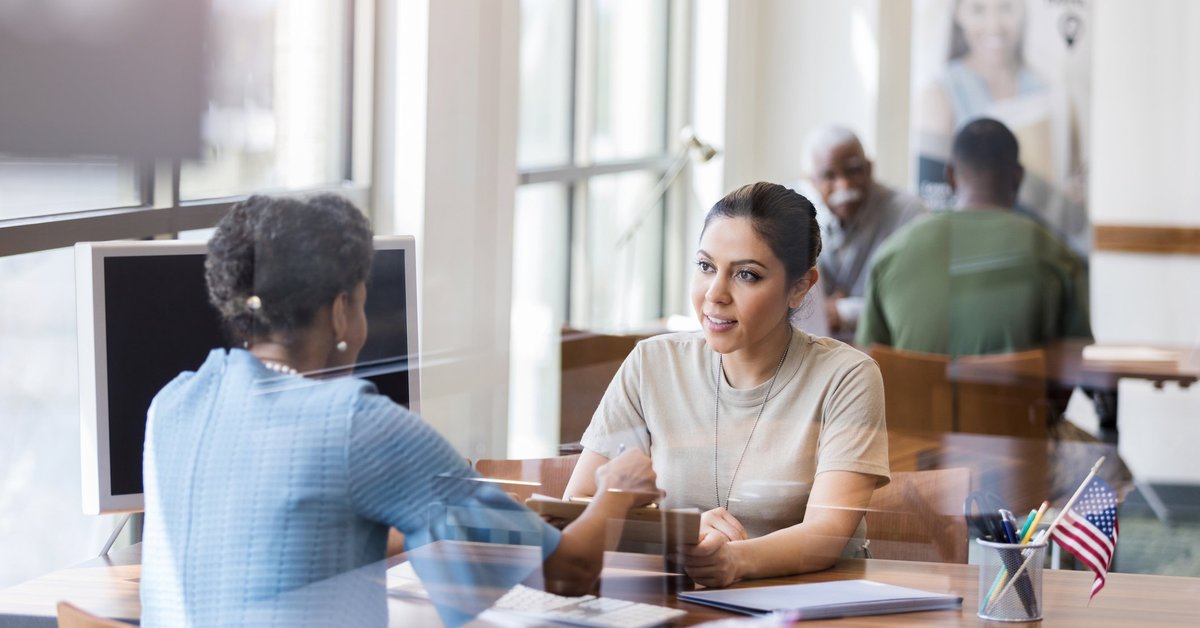 Two women sitting across a desk from one another in an office and discussing something important.