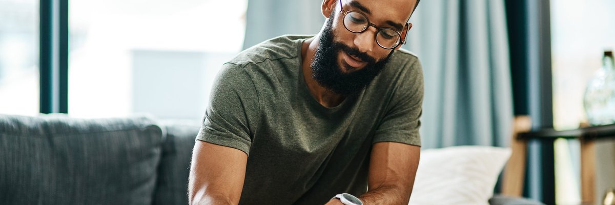 A buff, bearded, bespectacled young man looking relaxed and confident while marking something down on a piece of paper.