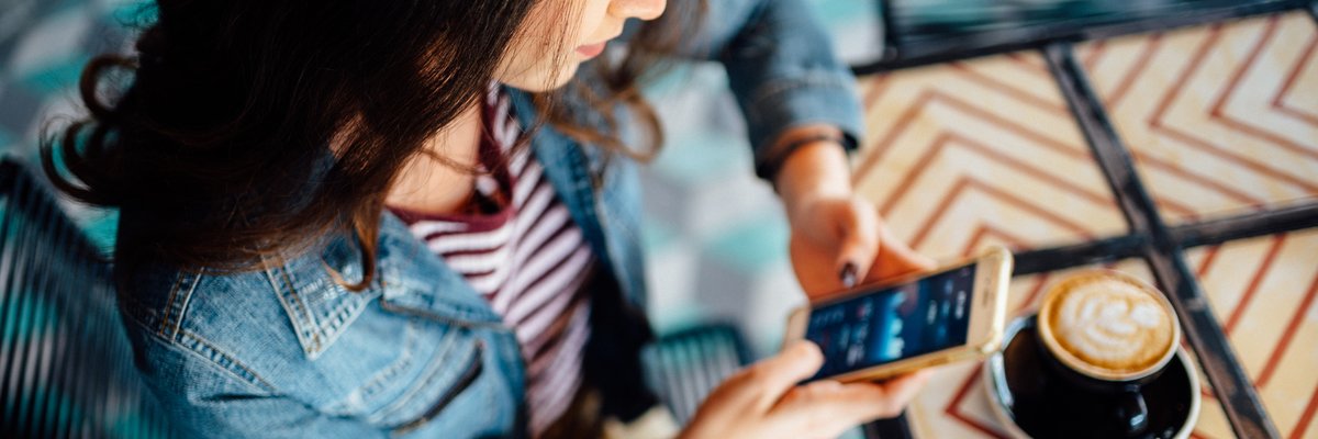 A person in a coffee shop looks at stock graphs on their smartphone.