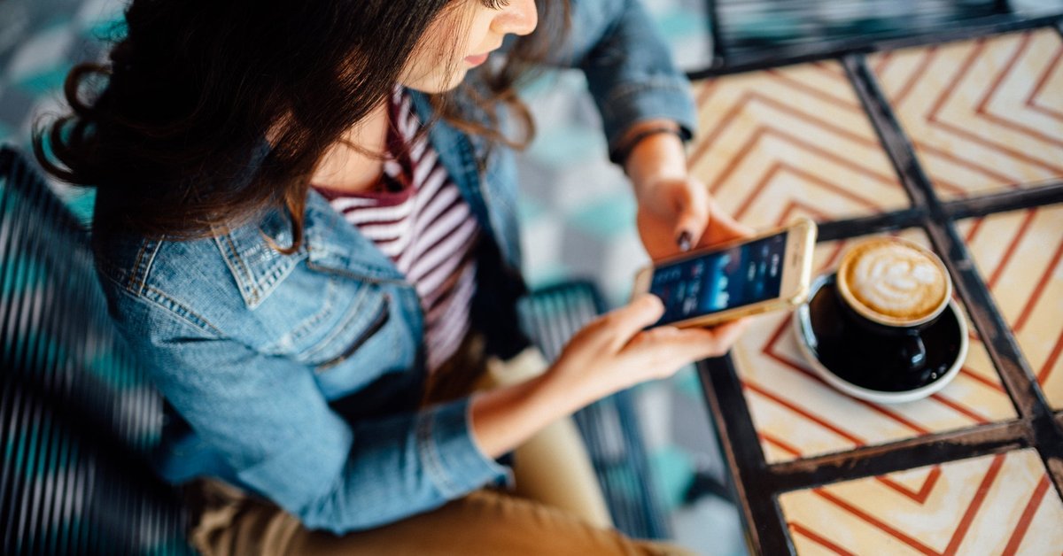 A person in a coffee shop looks at stock graphs on their smartphone.