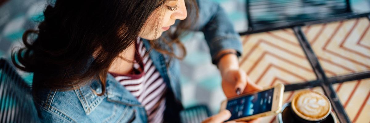 A person in a coffee shop looks at stock graphs on their smartphone.