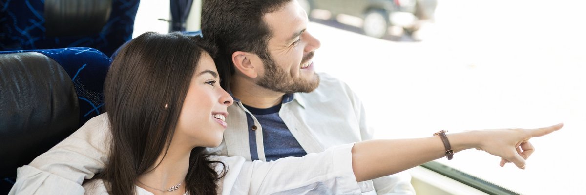 Young couple on a bus smiling and looking at something through the window.