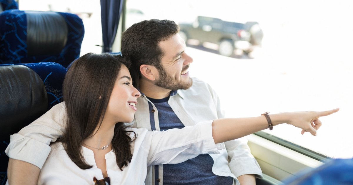 Young couple on a bus smiling and looking at something through the window.