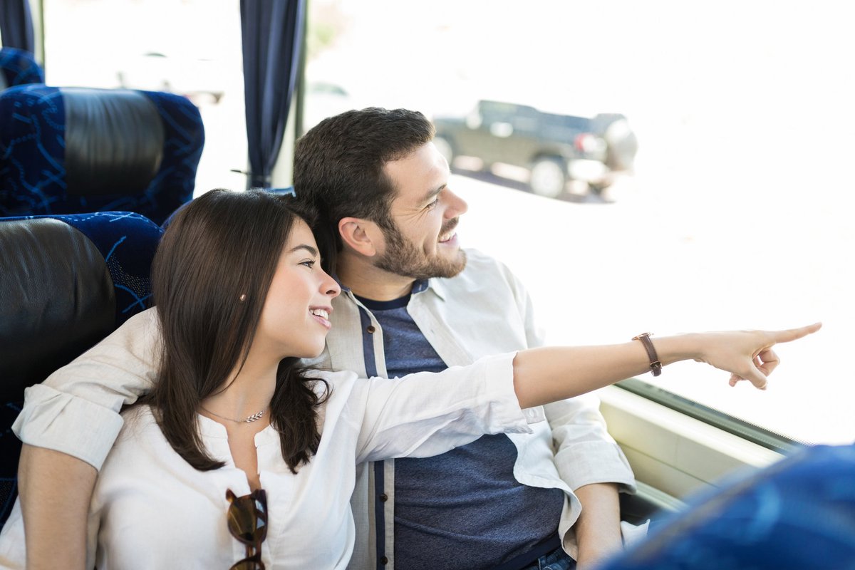 Young couple on a bus smiling and looking at something through the window.