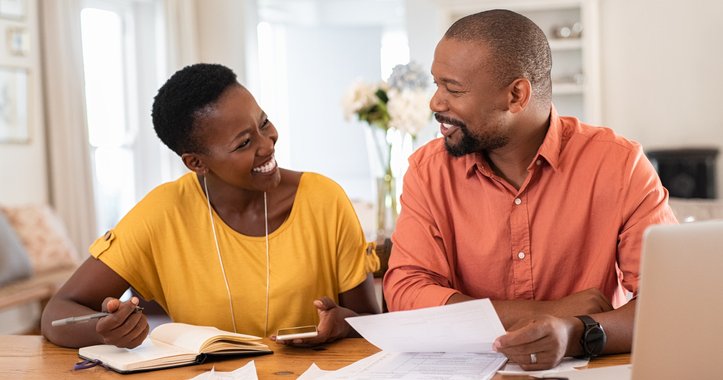 Happy couple reviewing paperwork at a desk with a laptop in their home