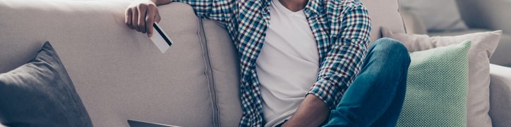 Smiling man sitting on sofa with laptop and credit card.
