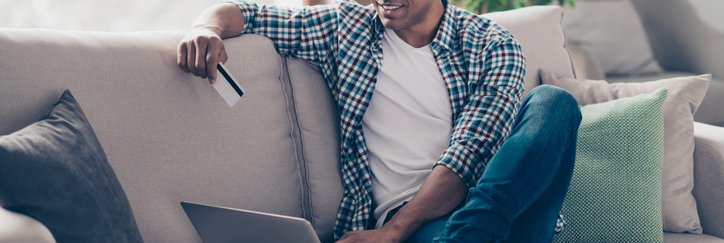 Smiling man sitting on sofa with laptop and credit card.
