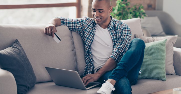Smiling man sitting on sofa with laptop and credit card.