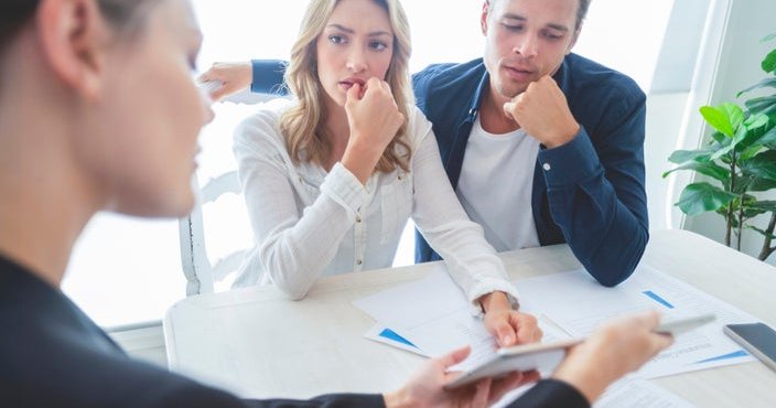 Real estate agent and worried couple look through documents.