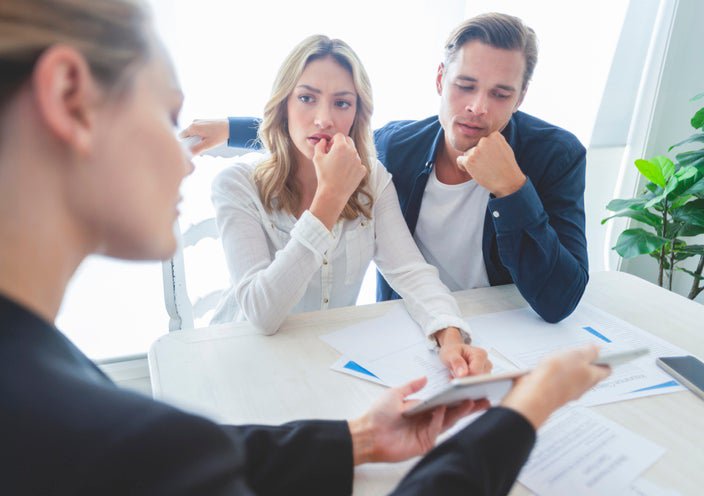 Real estate agent and worried couple look through documents.